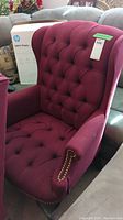 Front view of the burgundy wingback chair showing tufted back and brass nailhead trim on arm.