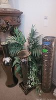 Full lot view showing faux plant with green leaves and trailing vines, two tall shiny metallic vases with textured patterns, and two metallic candle holders