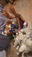 Image showing bundles of dried faux wheat stalks, white roses and other flowers, and white dried flower arrangements.