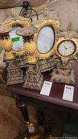 Wide view of the full set on a wooden table showing two photo frames, two candle holders, and a clock with eagle designs and ornate bases
