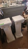 Two white classical pedestals shown side by side with visible fluted column shafts and square tops and bases.