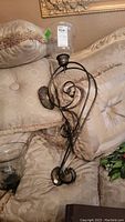 Side view of one metal wall sconce with ornate dark metal scrollwork and a clear glass hurricane shade, laid on pillows.