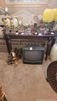 Full view of wooden sofa table with various decorative items on top and a TV on the floor beneath it.