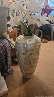 Full view of tall mosaic vase with white faux flowers inside, showing overall shape, material pattern and color.