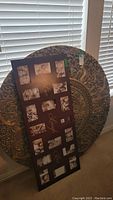 Photo showing the large round decorative metal wall medallion with embossed floral and geometric design leaning against a wall along with a multi-photo wall frame.