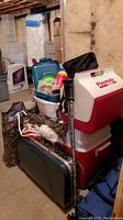 Stacked camping gear in basement including coolers, walking sticks, ropes, plastic bins, and a camouflage tent bag