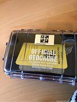 Photo of official geocache container inside a sealed clear hard case with label 'Official Geocache Please Do Not Disturb'.