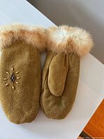 Top and underside views of light brown mittens with fur trim and bead decoration on one mitten.