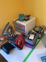 Image showing a workspace corner with plastic storage drawers, several pencil cases with various pens and markers, a ruler, and organization boxes.