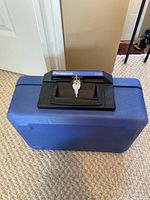 Blue SentrySafe 1100 fire safe closed with keys in lock, black handle on top.