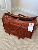 Front view of brown leather satchel showing main compartment, handles, and front pocket with buckle.