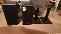 Two B&W 600 Series i speakers and two black metal stands on a basement floor