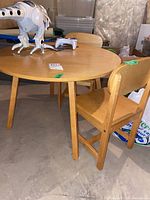 Round wooden child's table with two matching chairs placed on concrete basement floor, showing overall set and condition with light wear.