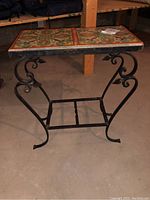 Full view of metal framed tile table showing metal scrollwork legs and tile top with colorful floral pattern.