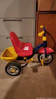 Side view of child's tricycle with red seat, blue frame, and yellow basket at rear