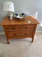 Front view of vintage wooden dresser with two drawers, top holding lamp and ceramic bowl