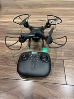 Black quadcopter drone with propeller guards and remote controller on wooden floor