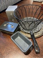 Seven items shown on wooden floor including baking pans, wire basket, and metal storage tins