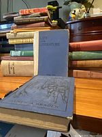 Stack of vintage books on a table, focus on a blue hardcover book titled 'Life and Literature' and other aged books behind.