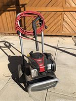 Full view of gas powered pressure washer with coiled red hose on handle and black/red Briggs & Stratton engine.