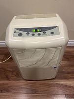 Front view of white Maytag dehumidifier with control panel showing power and settings buttons, unit placed on wooden floor.