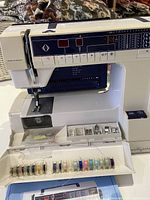 Husqvarna Prisma 950 sewing machine with multiple colored thread spool set in front and various sewing attachments in compartment below needle area