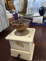 Side view of vintage manual coffee grinder showing wooden base, metal grinding bowl, and black knob on handle.