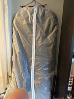 Garment bag containing the coat, closed with white zipper.