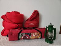 Lot contents showing tent in carrying case, red sleeping bag, Eddie Bauer cooler backpack, and green lantern