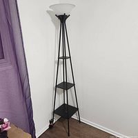 Full view of the black corner floor lamp in a corner, showing triangular shelves and frosted glass shade at top.