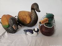 Four duck items laid out on white surface: two brass and glass duck lamps, one carved wooden duck, and one decorative glass duck figurine.
