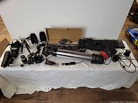 Wide view of all electronics and gear on table including keyboard, camera, tripod, webcam, media player, cables, and accessories.