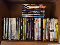Photo showing an open box with 35+ family, kid, and comedy movie DVDs arranged lying flat and standing.