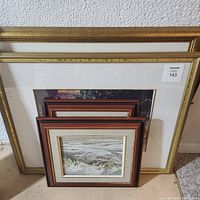Photo of stacked framed prints showing size and frame styles, includes largest frame at back with gold edging and smaller frames in front with wood and beige matting.
