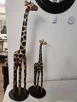 Full view of both tall and smaller giraffe sculptures side by side, showing height difference and bases.