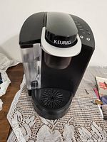 Front/view showing water reservoir, handle with Keurig logo, drip tray, control panel with buttons.