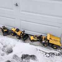 Four metal Tonka trucks lined up in a row outside on snow and concrete, showing general size and condition.