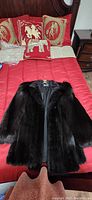 Full view of the dark mink fur jacket laid on red bedspread showing front with collar and sleeves.