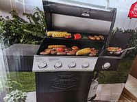 Assembled grill on packaging showing cooking grate loaded with food and side burner in use