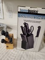 Photo showing a used wooden knife block with several knives, placed next to its original boxed set labeled HomeBasics 10-piece cutlery set.