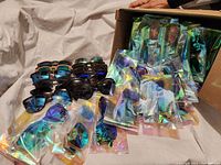 Box of individually wrapped Optimum Optical sunglasses with some unwrapped pairs displayed