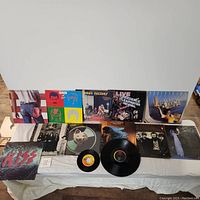 Photo of multiple classic rock vinyl records placed on a white cloth. Visible albums include Bruce Springsteen, Queen, The Who, Creedence Clearwater Revival, Kiss, and others, some with vinyl records removed or partially visible.