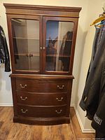 Front view of the small wooden display hutch with closed glass doors and drawers visible.