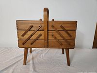 Closed view of a vintage wooden sewing basket showing wood grain, central handle, and four legs