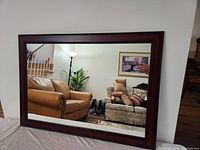 Full view of large wall mirror showing the brown frame and clear mirror reflecting a living room interior.