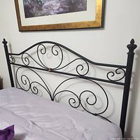 Full view of black wrought iron headboard mounted on wall with purple bedding below