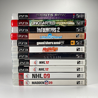 Photo of 11 PS3 game cases stacked horizontally showing spines with titles including Saints Row The Third, Uncharted Drake's Fortune, Infamous 2, Little Big Planet, Grand Theft Auto V, Mod Nation Racers, Skyrim, NHL 12, NHL 09, and Madden NFL 09.
