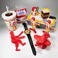 Photo showing 8 vintage McDonald's Ronald McDonald-themed items including toys, watch, cup, paper bag, and plastic tray