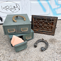 Overall view of the lot showing two steel file card drawers, two horseshoes, and a decorative heating vent register against a graffiti wall.