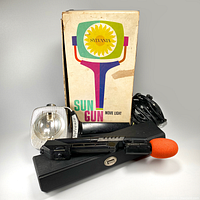 Sylvania SG-50 Sun Gun movie light with attached cord, original box, and GAF microphone with orange foam windscreen and black carrying case arranged together.